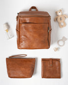 Brown vegan leather backpack, pouch, and wallet on a white background with baby items.
