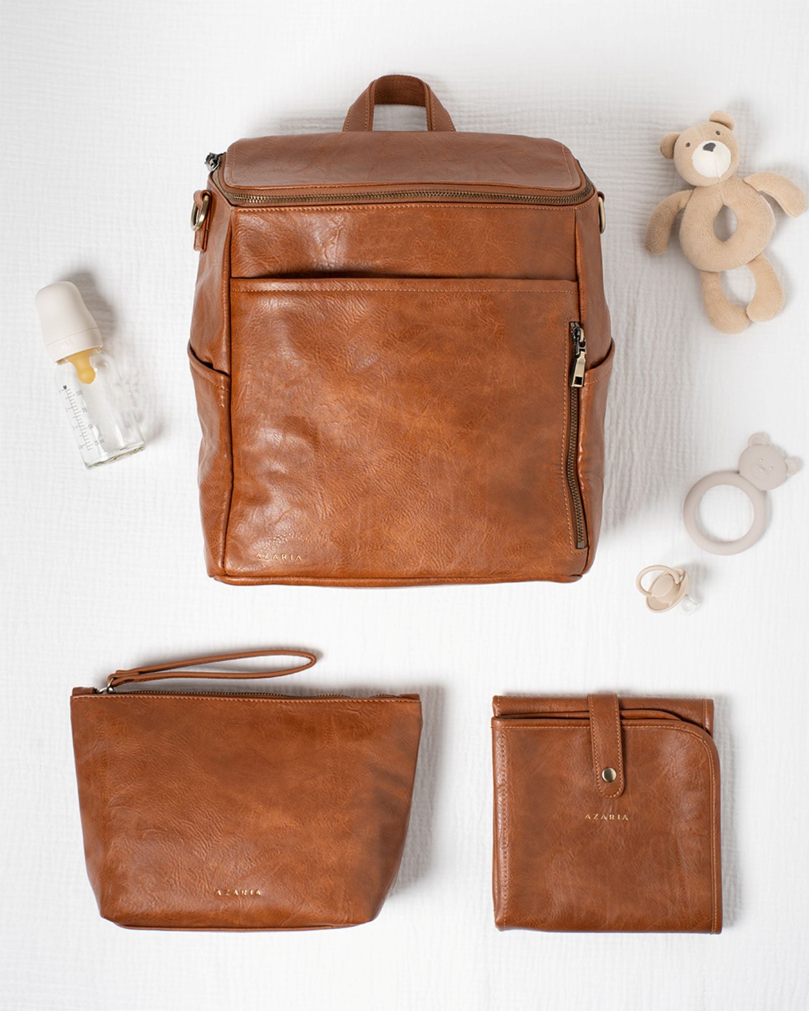 Brown vegan leather backpack, pouch, and wallet on a white background with baby items.